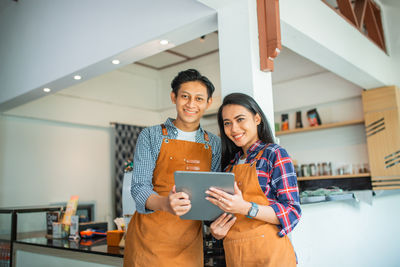 Portrait of smiling young woman using digital tablet while standing in office