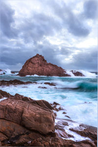 Rock formations by beach against cloudy sky