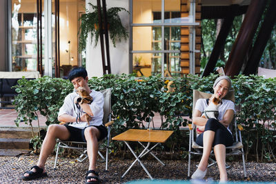 Asian couple holding a small dog sitting on a chair in garden outdoor.