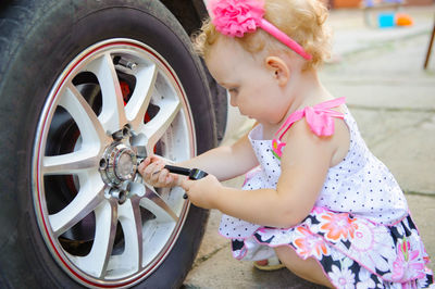 Full length of cute girl holding tool by car