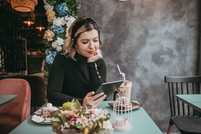 Young woman using phone while sitting on table