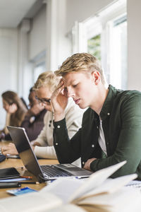 Serious young man using laptop in classroom