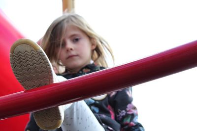 Low angle portrait of girl climbing on ladder against clear sky at playground