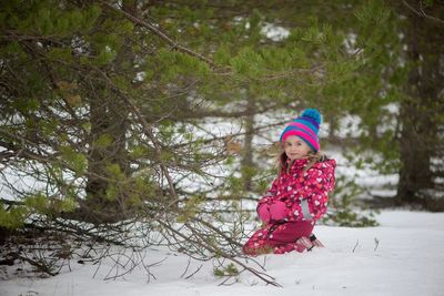 Portrait of girl smiling while sitting on snowy field by trees