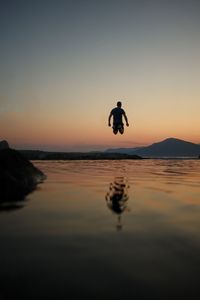Rear view of man jumping at beach against sky during sunset