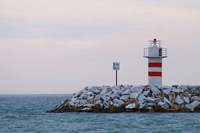 Lighthouse by sea against sky during sunset