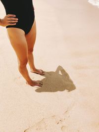 Low section of woman with hand on hip standing at beach