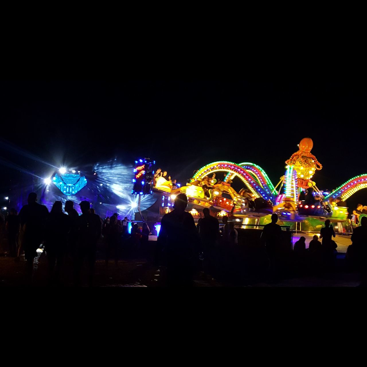 ILLUMINATED PEOPLE AT AMUSEMENT PARK AGAINST SKY