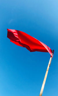 Low angle view of red flag against clear blue sky