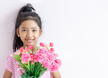 Portrait of smiling girl with pink flower against white background