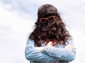 Woman wearing sunglasses while covering face with hair against sky