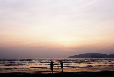 Silhouette people standing on beach against sky during sunset