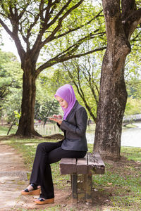 Young woman wearing hijab using mobile phone while sitting in park