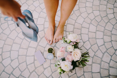 Low section of woman holding high heels over bouquet on footpath