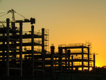 Silhouette cranes at construction site against sky during sunset