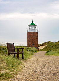 Lighthouse on field by building against sky