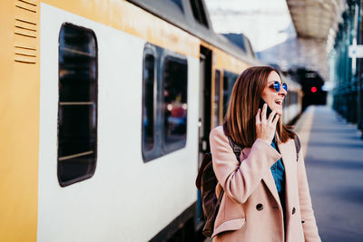 Woman with phone standing by train on railroad station platform