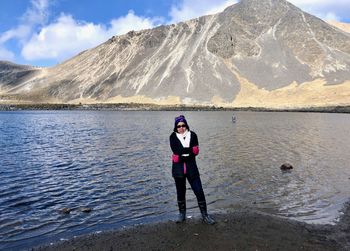 Full length portrait of man standing by lake against mountain