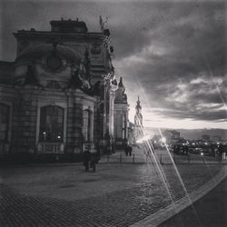 People walking in city against cloudy sky