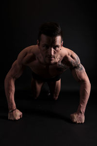 Portrait of shirtless athlete doing push-ups against black background