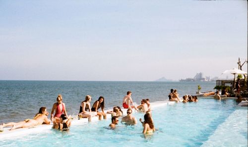People relaxing in infinity pool against sky