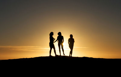 Silhouette women standing on hill against sky during sunset