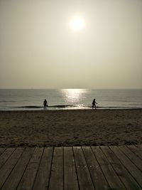 Silhouette people standing on beach against clear sky during sunset