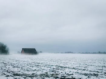 House on snow covered field against sky during winter