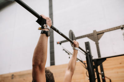Cropped unrecognizable fit male athlete doing pull ups on bar during workout in contemporary gym