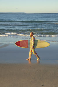 Mid adult man in suit walking with surfboard against sea