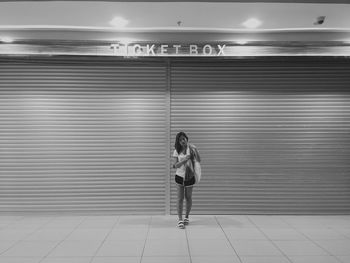 Full length portrait of young woman standing against shutter at night