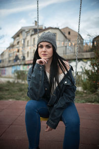 Young woman wearing denim jacket sitting on swing at playground