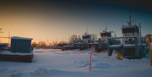 Houses by snow covered buildings against sky during sunset