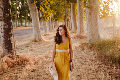 Young woman standing by tree trunks in forest