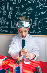 Boy wearing lab coat while mixing chemicals in classroom