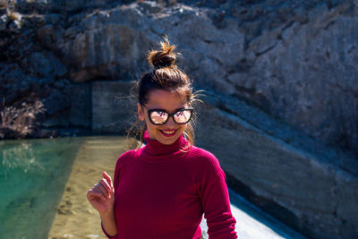 Portrait of smiling woman wearing sunglasses while standing at poolside 