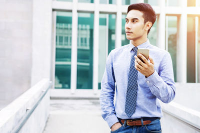 Businessman holding mobile phone while standing in city