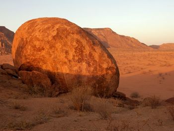 Red rock boulder in desert against sky at sunset