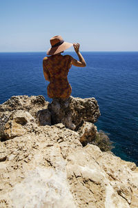 Man on rock by sea against sky