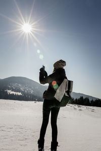 Side view of female hiker photographing with mobile phone while standing on snow covered field