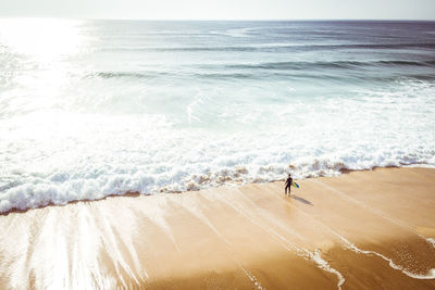 Scenic view of sea with man holding surfboard while standing at beach against sky