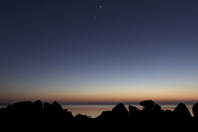 Silhouette rocks and sea against sky at dusk