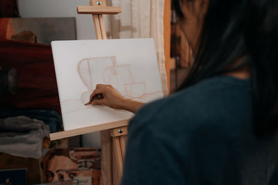 Crop anonymous female artist using brush to paint cup and jar while working in professional workshop