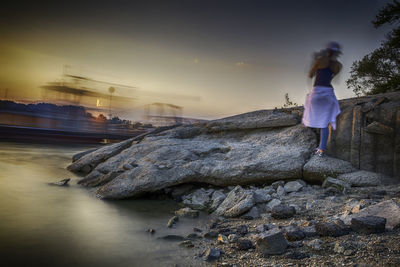 Rear view of woman standing on rock by sea during sunset