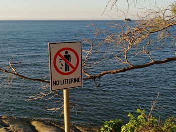 Information sign by sea against sky