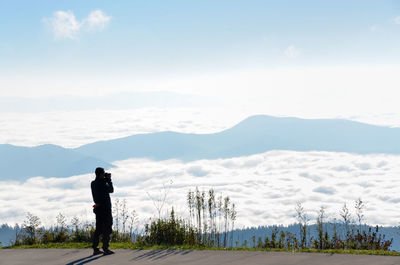 Rear view of man photographing on mountain against sky