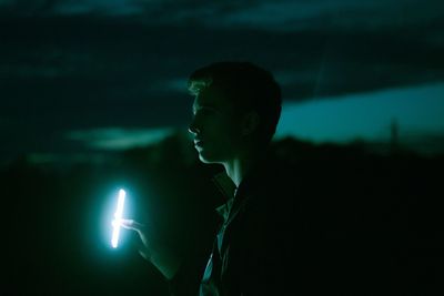 Side view of young man holding mobile phone at night