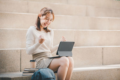 Young woman using digital tablet sitting on steps outdoors