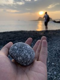 Cropped hand holding stone at beach during sunset