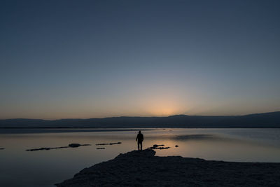 Silhouette man standing on shore against clear sky during sunset